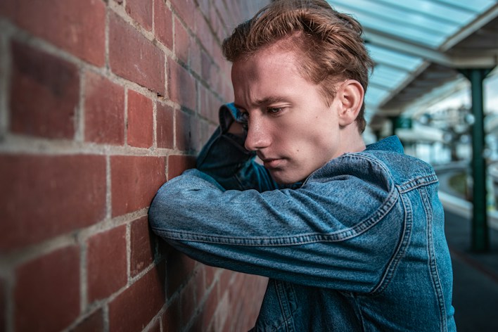 Exhausted young man leaning against a brick wall