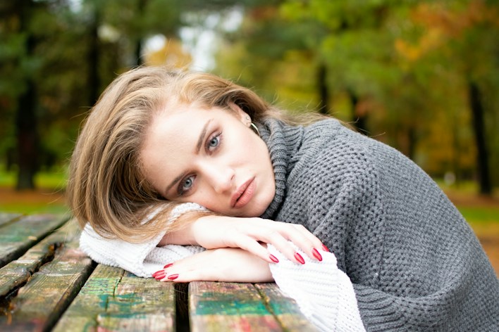 Young woman resting her head on a park table, looking tired